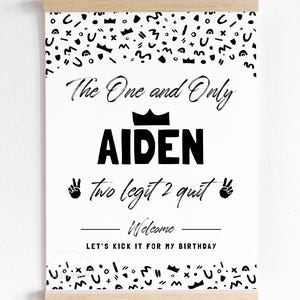 May include: A white rectangular poster with black text and abstract shapes, held by a wooden magnetic frame. The text reads: The One and Only AIDEN, two legit 2 quit, Welcome, LET'S KICK IT FOR MY BIRTHDAY, featuring crown and peace sign icons.