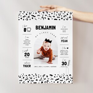 May include: A black and white first birthday milestone poster with a photo of a baby boy wearing a crown. The poster includes the baby's name, Benjamin, and details about his first year, including his weight, height, and first words. The poster is decorated with a black and white geometric pattern.
