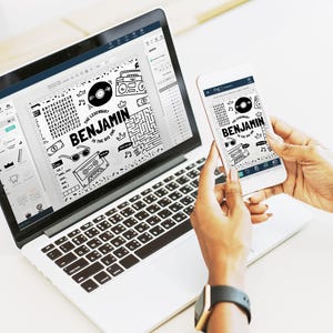 May include: A silver laptop and a white smartphone displaying a black and white graphic design featuring the text "THE LEGENDARY BENJAMIN IS THE BIG ONE" surrounded by illustrations of a vinyl record, a boombox, sunglasses, and a maze pattern.
