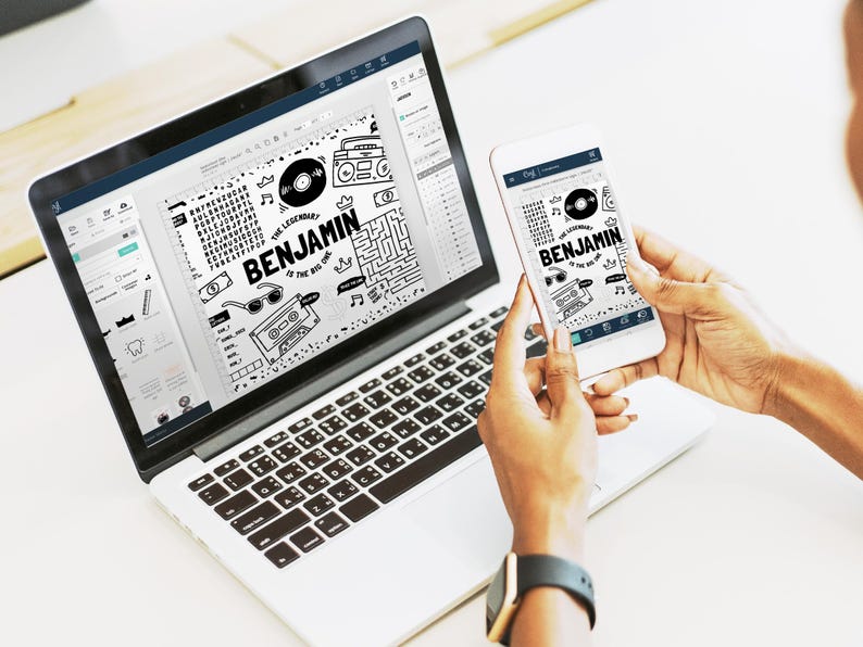 May include: A silver laptop and a white smartphone displaying a black and white graphic design featuring the text "THE LEGENDARY BENJAMIN IS THE BIG ONE" surrounded by illustrations of a vinyl record, a boombox, sunglasses, and a maze pattern.