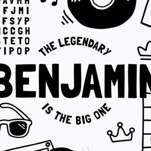 May include: A white graphic print featuring the black text BENJAMIN IS THE BIG ONE in the center, surrounded by black line art illustrations including sunglasses, a crown, a vinyl record, and a word search puzzle grid on a white background.