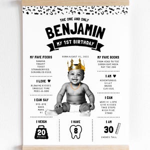 May include: A white poster with black text and graphics featuring a baby wearing a gold crown and chain. The text includes THE ONE AND ONLY BENJAMIN MY 1ST BIRTHDAY, birth date, favorite foods, books, personality traits, skills, 20 pounds, 8 teeth, and 30 inches tall.