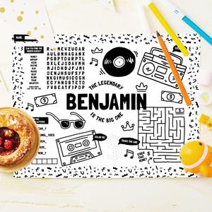 May include: A black and white activity sheet featuring the text "THE LEGENDARY BENJAMIN IS THE BIG ONE" surrounded by illustrations of a vinyl record, boombox, sunglasses, cassette tape, maze, crowns, dollar bills, and a word search puzzle.