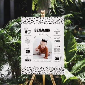 May include: A black and white first birthday milestone poster with a photo of a baby boy wearing a crown. The poster features the baby's name, Benjamin, and details about his first year, including his weight, height, and first words. The poster is decorated with a black and white geometric pattern.