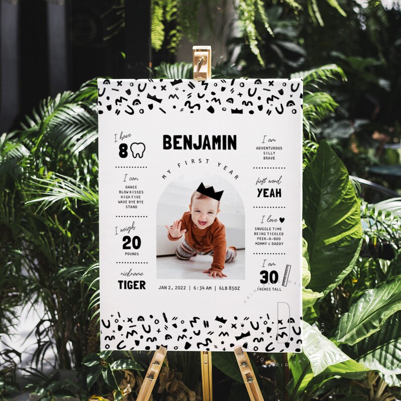 May include: A black and white first birthday milestone poster with a photo of a baby boy wearing a crown. The poster features the baby's name, Benjamin, and details about his first year, including his weight, height, and first words. The poster is decorated with a black and white geometric pattern.