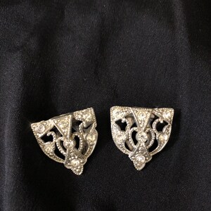 May include: A pair of silver shoe buckles with a decorative design and clear rhinestones.