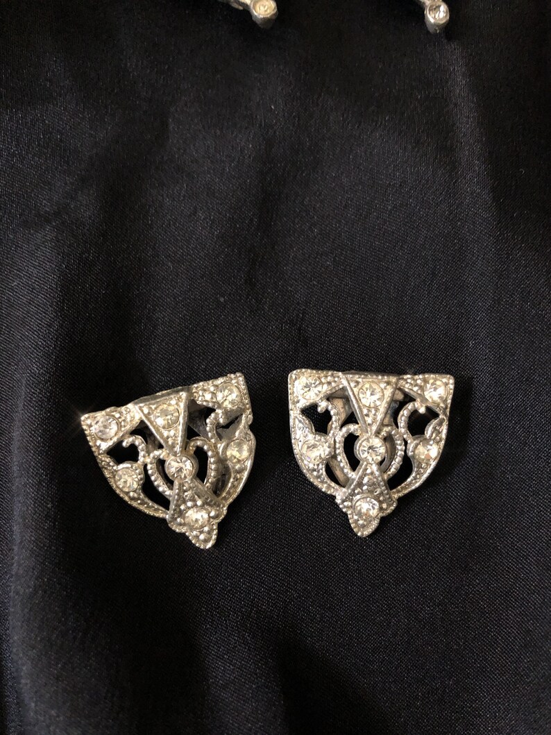 May include: A pair of silver shoe buckles with a decorative design and clear rhinestones.