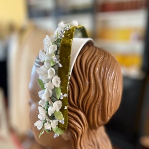 May include: A white headband with a green velvet ribbon and white flower embellishments.