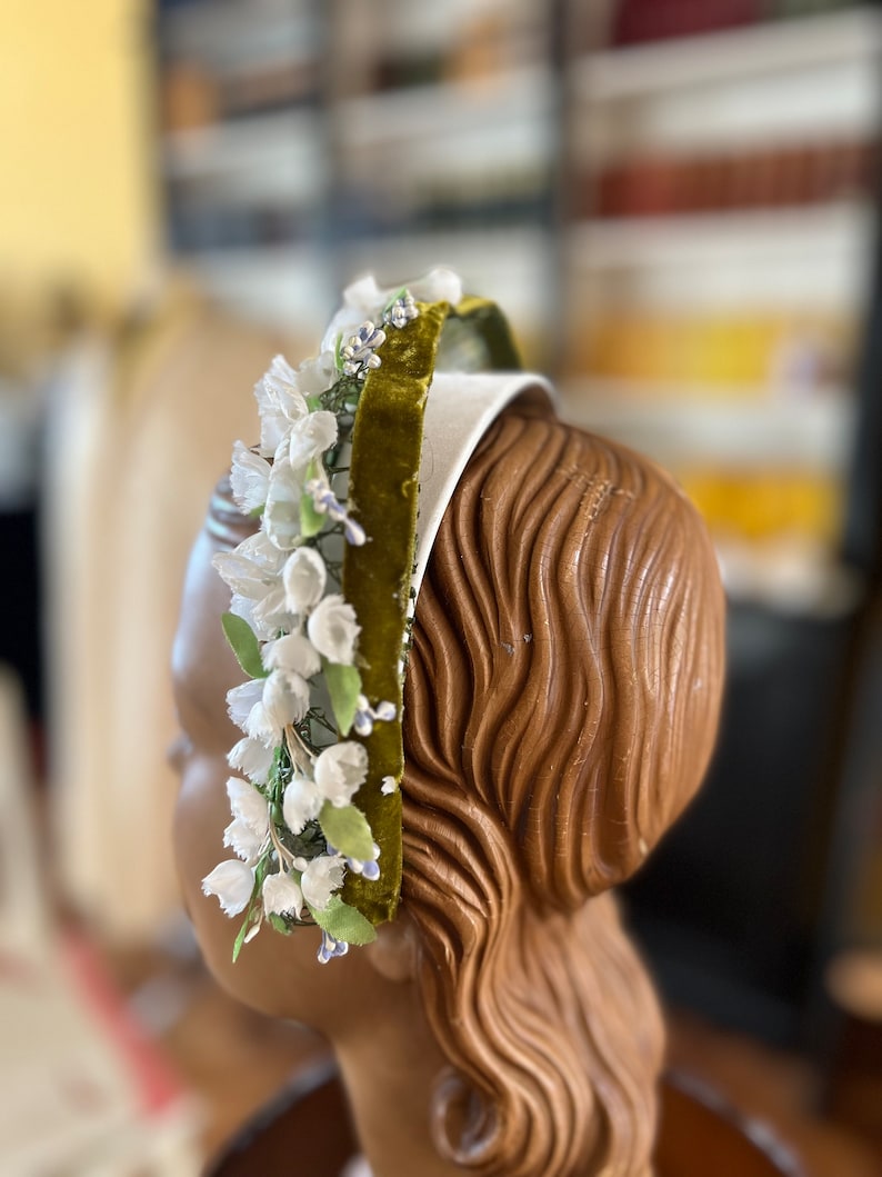 May include: A white headband with a green velvet ribbon and white flower embellishments.