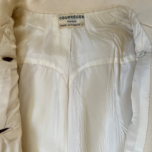 May include: A white jacket with a label that reads "Courr&egrave;ges Paris Made in France C".