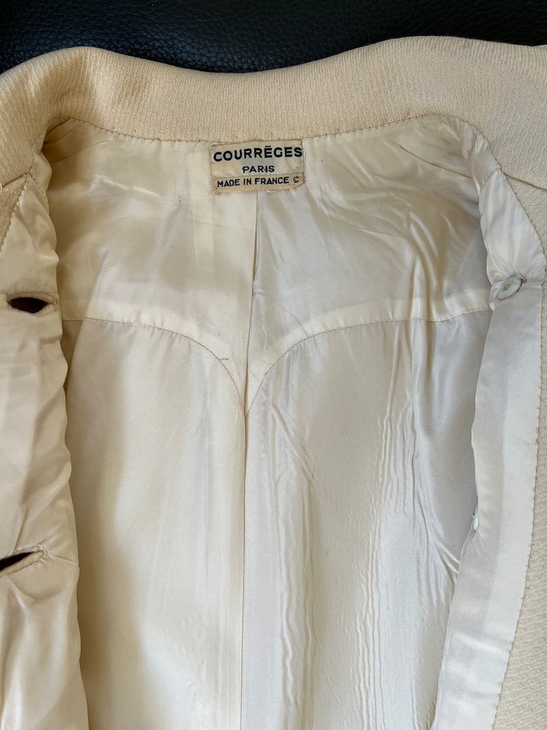 May include: A white jacket with a label that reads "Courr&egrave;ges Paris Made in France C".