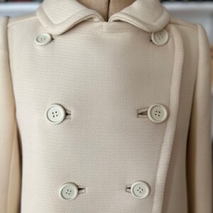 May include: A cream-colored double-breasted coat with a large collar and six white buttons.