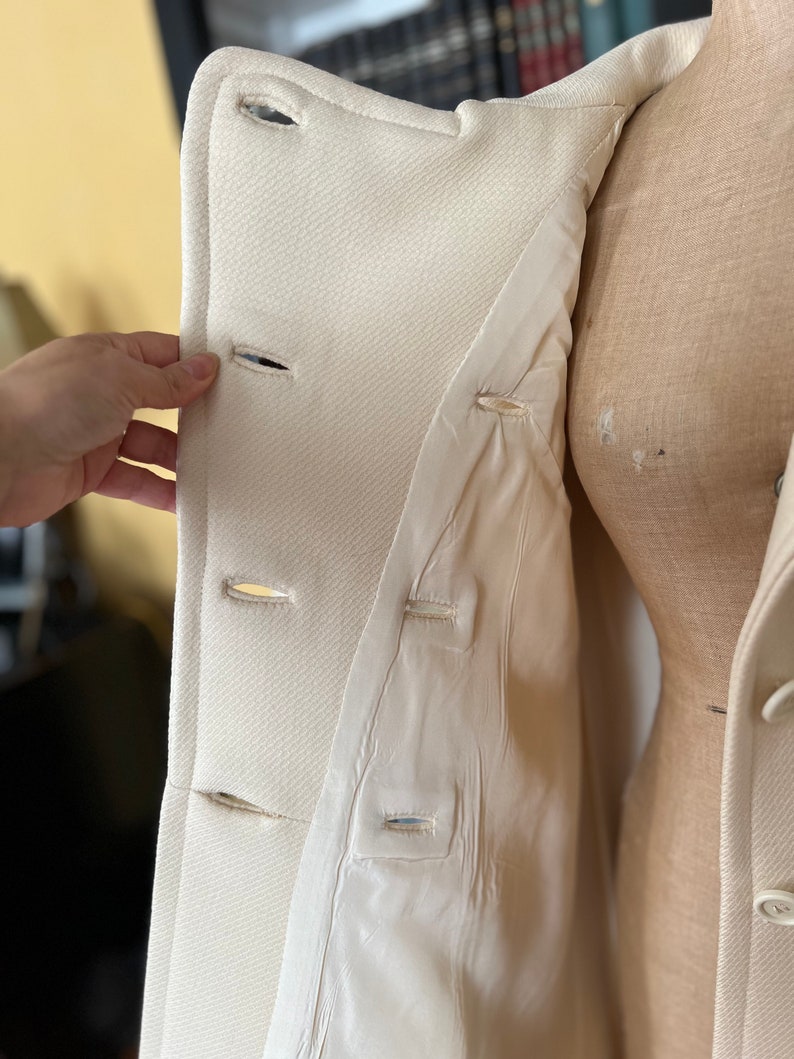 May include: A white double-breasted coat with a button closure. The coat is open and the lining is visible. The lining is also white.