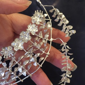 Puede incluir: Un collar de plata con un delicado dise&ntilde;o floral. El collar presenta un grupo de peque&ntilde;as flores y hojas, creando un look delicado y femenino.