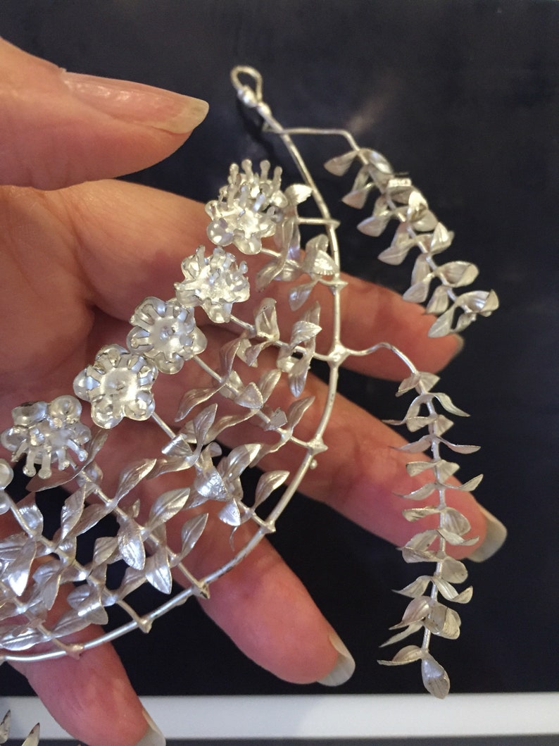 Puede incluir: Un collar de plata con un delicado dise&ntilde;o floral. El collar presenta un grupo de peque&ntilde;as flores y hojas, creando un look delicado y femenino.