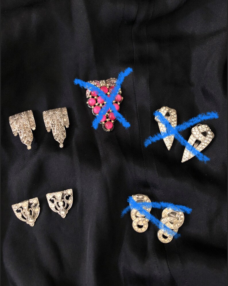 May include: A set of five vintage silver-toned brooches with rhinestones. Two brooches are shaped like a teardrop, one is a cluster of pink stones, and two are shaped like a rectangle.
