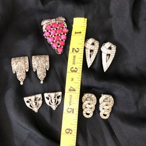 May include: A set of seven vintage silver-toned metal brooches with rhinestones. One brooch features a cluster of pink glass stones in the shape of a grape bunch.  The other brooches are various geometric shapes.