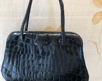 May include: A black crocodile embossed leather handbag with a top handle.
