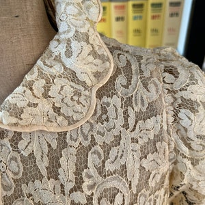 Puede incluir: Una blusa de encaje blanco con cuello festoneado. El encaje es delicado e intrincado, con un patr&oacute;n floral.