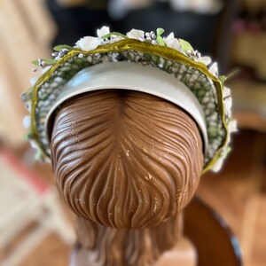 May include: A white headband with a green velvet ribbon and white and purple flower accents.