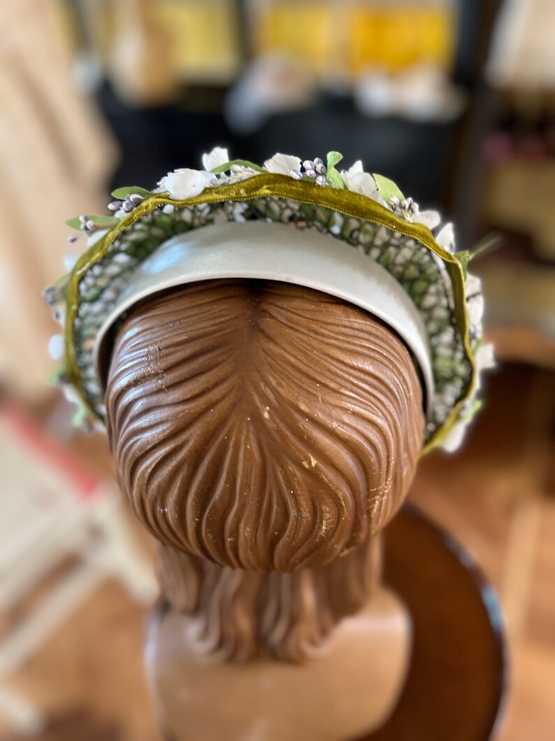 May include: A white headband with a green velvet ribbon and white and purple flower accents.
