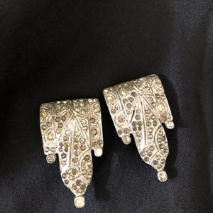 May include: A pair of silver earrings with a geometric design, featuring a cascade of small, clear rhinestones.