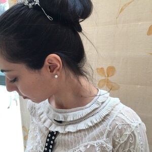 Puede incluir: Una mujer con el pelo oscuro recogido en un mo&ntilde;o con un peine de pelo plateado. Lleva una blusa blanca de encaje con una cinta de terciopelo negro y botones blancos.