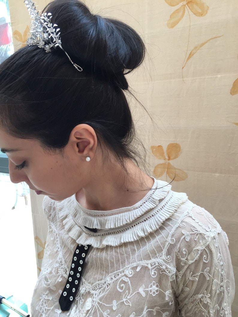 Puede incluir: Una mujer con el pelo oscuro recogido en un mo&ntilde;o con un peine de pelo plateado. Lleva una blusa blanca de encaje con una cinta de terciopelo negro y botones blancos.
