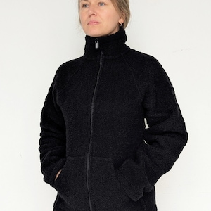 May include: A black fleece jacket with a high collar and a full-length zip. The jacket features two front pockets and is made of a textured, fuzzy material. The model is wearing blue jeans.