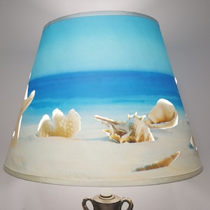 May include: A blue and white lampshade with a beach scene and seashells. The lampshade has cutouts in the shape of seashells.