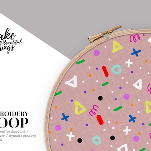 Puede incluir: Un bastidor de bordado con una tela rosa claro con formas geométricas coloridas. Las formas incluyen triángulos, círculos, signos más y garabatos en varios colores. El bastidor de madera es parcialmente visible, y el texto "Make Beautiful Things" está en la esquina superior izquierda.