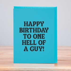 May include: A blue card with the text "Happy Birthday to one hell of a guy!" in black lettering.