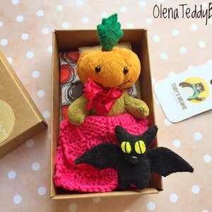 May include: A Halloween-themed teddy bear in a box. The bear is dressed as a pumpkin with a red bow and pink blanket. A black felt bat with yellow eyes sits in front of the bear. The box has a "Thank You" sticker.
