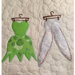 May include: Two fabric dresses on hangers, one green with white polka dots and one white with a sparkly design.