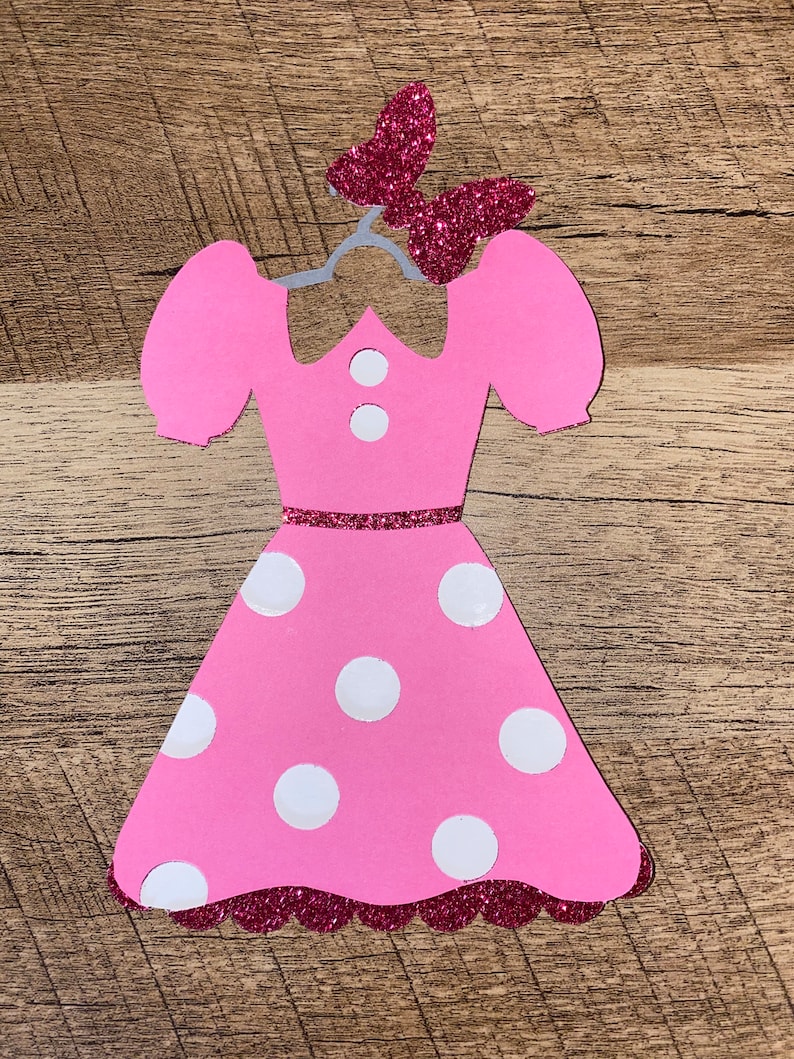 Puede incluir: Vestido de papel rosa con lunares blancos y un lazo rosa brillante en la parte superior. El vestido tiene un dobladillo festoneado y un cintur&oacute;n rosa brillante.