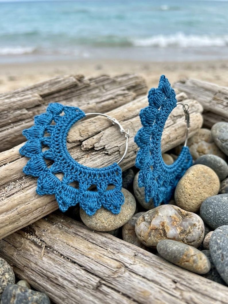 May include: A pair of hoop earrings featuring deep blue crochet thread wrapped around silver-toned metal hoops. The crochet work creates a scalloped, fan-like edge with textured, raised stitches along the outer perimeter of each circular earring.