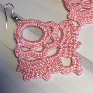 May include: A pair of pink crocheted earrings with a delicate, intricate design. The earrings are lightweight and feature a simple hook closure.