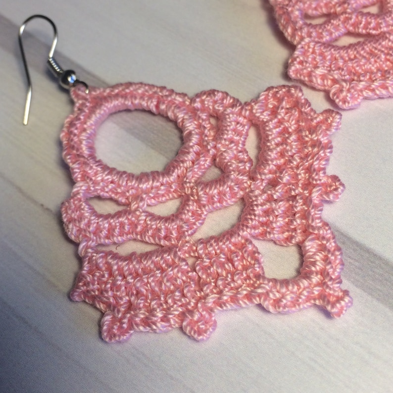 May include: A pair of pink crocheted earrings with a delicate, intricate design. The earrings are lightweight and feature a simple hook fastening.