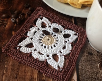 May include: A square crochet coaster featuring a dark brown border, a white floral-inspired centre pattern, and a small beige circular core. The intricate needlework creates a geometric design with open spaces between the white petals and the brown frame.