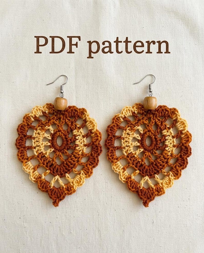 May include: A pair of heart-shaped crochet earrings featuring a brown and cream color scheme with a central wooden bead and silver-toned metal hooks. The text PDF pattern is displayed above the earrings in a brown sans-serif font.