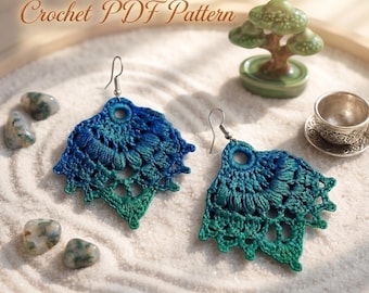 May include: A pair of crochet earrings featuring a gradient color scheme transitioning from deep blue at the top to emerald green at the bottom. The earrings have a fan-like shape with intricate openwork stitching and silver-toned metal hooks.