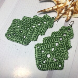 May include: A pair of green crocheted earrings with a delicate, lacy design. The earrings are made with a fine yarn and have a simple, elegant style.