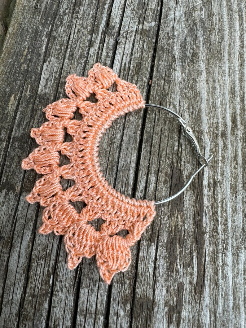 May include: Peach-colored crocheted earrings with a silver hoop and a hook closure.
