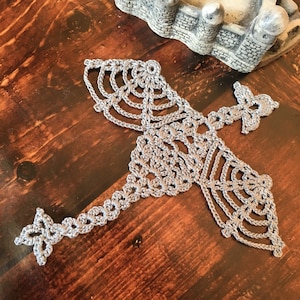 May include: A silver crocheted snowflake design with intricate details. The snowflake is made with a delicate, openwork pattern.