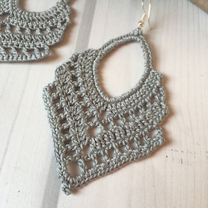 Puede incluir: Un par de pendientes de crochet plateados con un diseño delicado e intrincado. Los pendientes son ligeros y cuelgan de un gancho plateado.