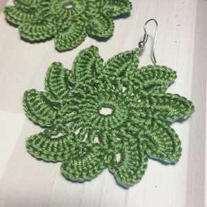 Pu&ograve; includere: Un paio di orecchini a forma di fiore fatti a crochet di colore verde con ganci argentati.