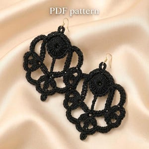 May include: A pair of black, handmade crochet earrings with a floral design. The earrings feature a circular center with intricate openwork patterns and gold-colored ear wires. The words "PDF pattern" are in the top center.