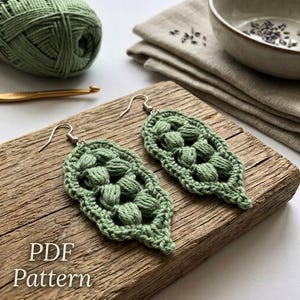 May include: A pair of sage green crochet earrings featuring a textured leaf-like shape with raised bobble stitches and silver-toned metal hooks. The text PDF Pattern is visible in the bottom left corner of the image, indicating a digital design guide.