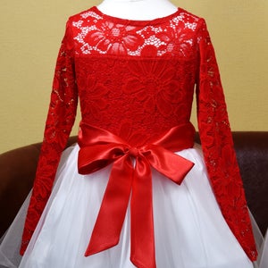 May include: A red lace dress with long sleeves and a white tulle skirt. The dress has a red satin bow at the waist.