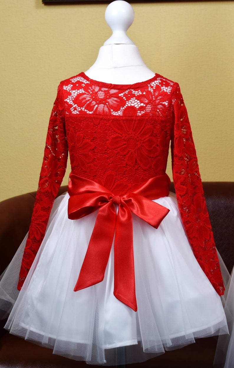 May include: A red lace dress with long sleeves and a white tulle skirt. The dress has a red satin bow at the waist.